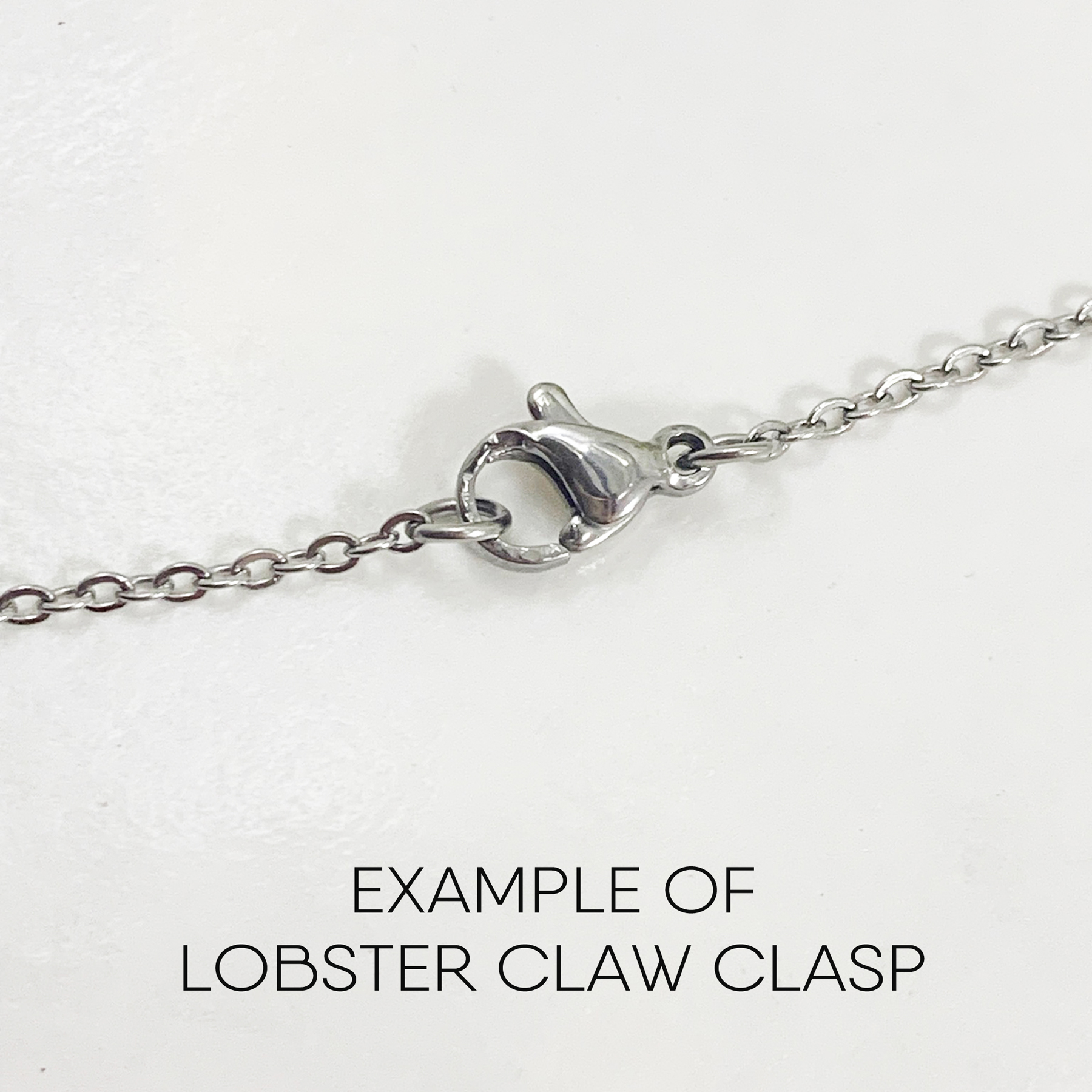 A close-up of a silver chain with a lobster claw clasp centered on a white background. Below the chain, "EXAMPLE OF LOBSTER CLAW CLASP" is written, demonstrating the clasp style used for the Boho Meditation Heart Necklace. Read more at Stamping Cat Studio (stampingcatstudio.com).