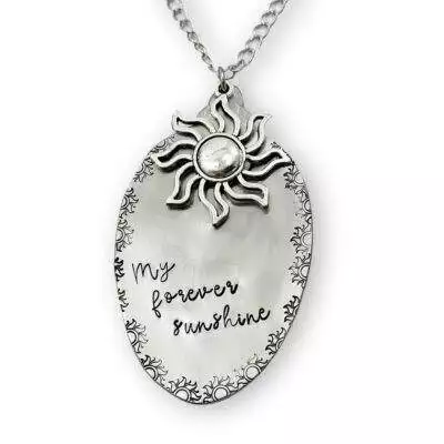 The Forever Sunshine Spoon Necklace features an oval silver pendant with a raised sun design, "My forever sunshine" handwritten-style engraving, ornate sun motif border, and hangs from a medium-length silver-toned chain. Read more at Stamping Cat Studio (stampingcatstudio.com).