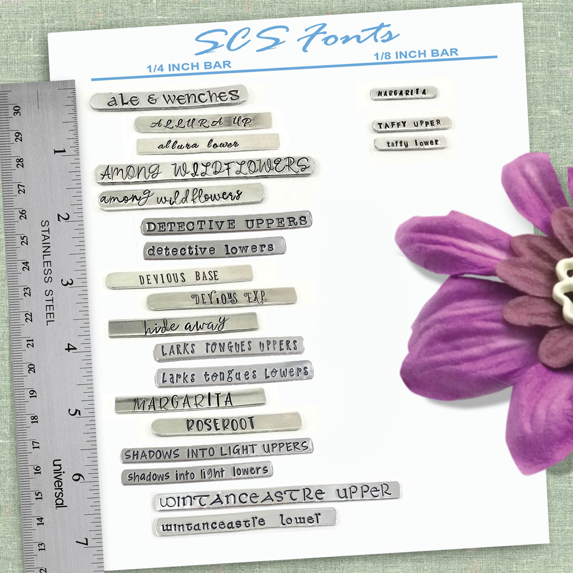 A sheet labeled “SCS Fonts” shows stamped silver metal bars in different fonts, each named. A metal ruler sits on the left for scale. A purple artificial flower and the Inspiring Butterfly Necklace complete the charming display. Read more at Stamping Cat Studio (stampingcatstudio.com).