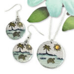 Dreamy Beach Scene set main includes round earrings and a necklace pendant with hand-painted turtle, palm tree, sun, waves, and sand designs. Displayed with a green paper leaf and blue flower for decoration. Read more at Stamping Cat Studio (stampingcatstudio.com).