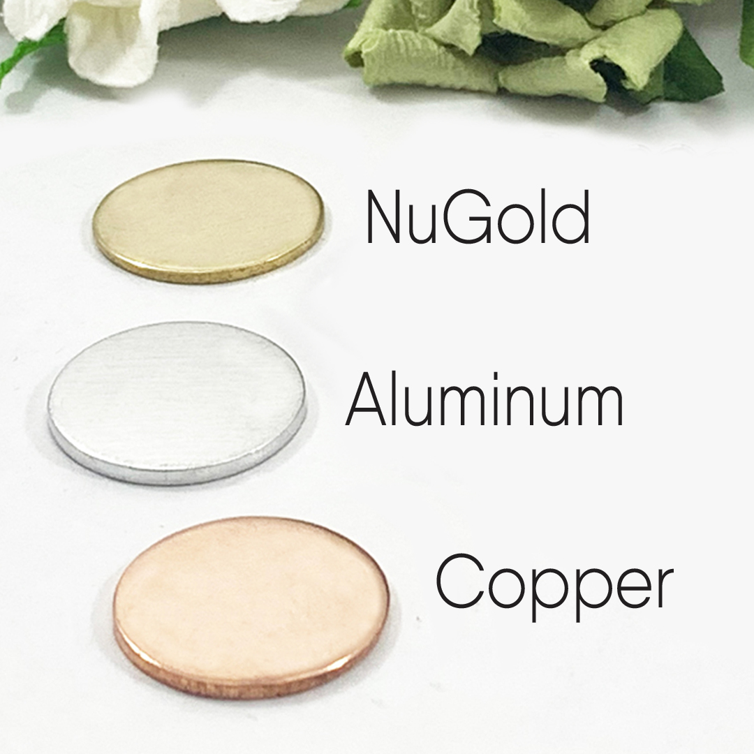 Three flat, round metal discs for the Kids Names Necklace For Mom are shown on a white surface with a floral background: the top disc is gold-colored (NuGold), the middle is silver (Aluminum), and the bottom is reddish (Copper). Read more at Stamping Cat Studio (stampingcatstudio.com).