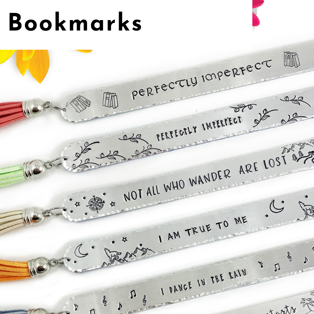 Five silver bookmarks with colored tassels are shown in a row. Each features hand-stamped text, like “PERFECTLY IMPERFECT,” along with decorative doodles—stars, moons, books, and branches—evoking the charm of personalized jewelry. Read more at Stamping Cat Studio (stampingcatstudio.com).
