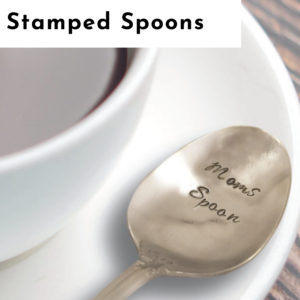A close-up of a silver spoon stamped with the words “Mom’s Spoon” rests on a white saucer beside a cup filled with dark beverage, evoking the charm of personalized jewelry. “Stamped Spoons” appears at the top left of the image. Read more at Stamping Cat Studio (stampingcatstudio.com).