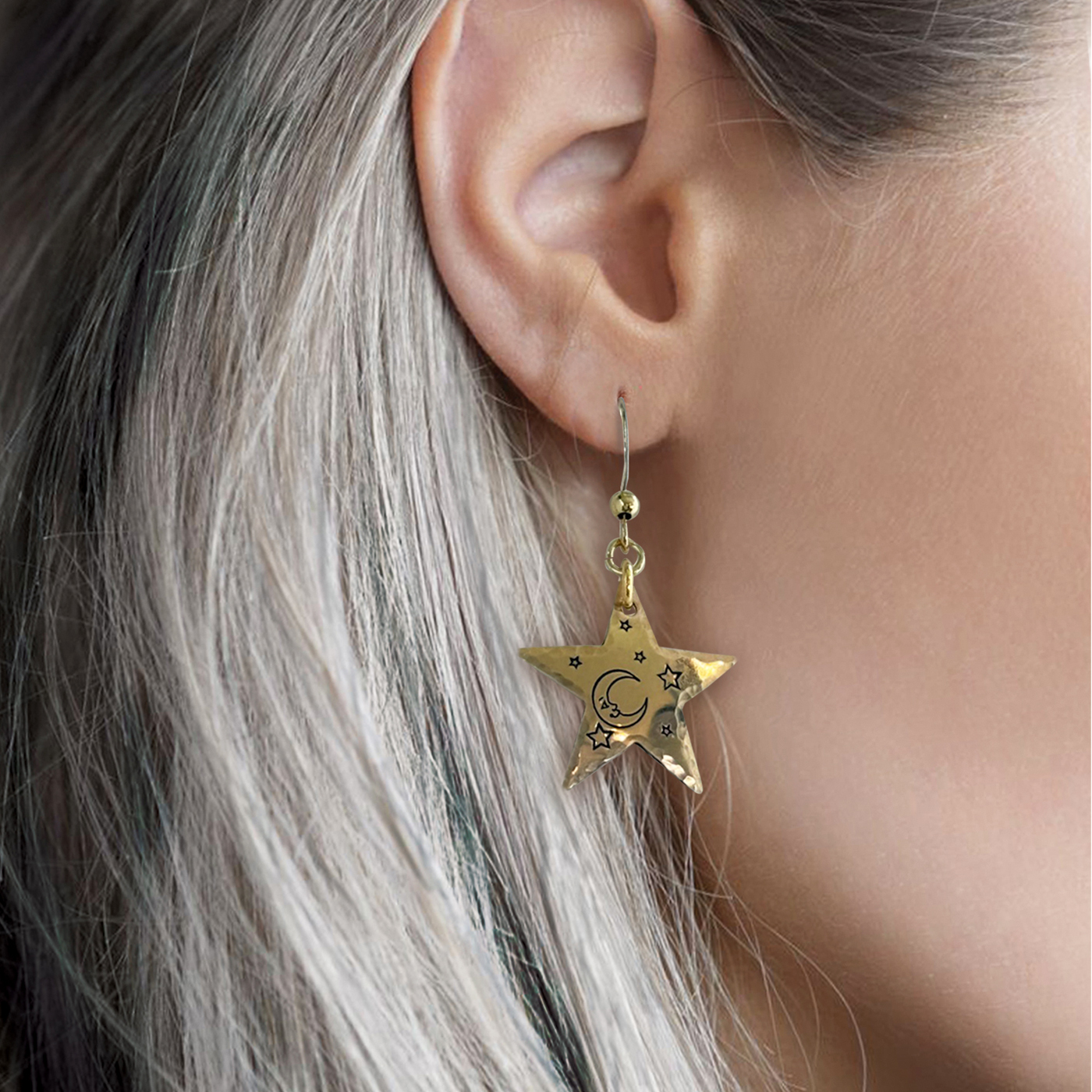 A close-up of a person’s ear with long, straight silver hair wearing the Bright Stars And Moon ear nugold, a gold star-shaped earring engraved with a crescent moon and small stars. A softly blurred background highlights its celestial design. Read more at Stamping Cat Studio (stampingcatstudio.com).