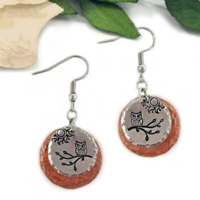 The "Owl On Branch MM ear main" are mixed metal earrings with silver hooks, featuring layered textured copper and smooth silver discs etched with an owl on a branch, accented by a sun charm, green leaves, and a cream flower background. Read more at Stamping Cat Studio (stampingcatstudio.com).