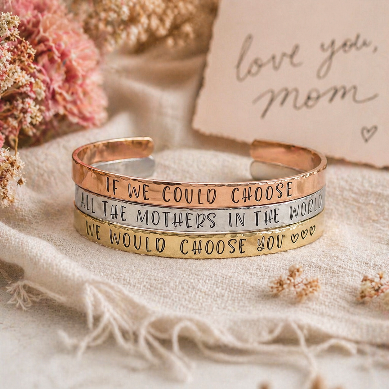 Three May 8 bracelets in rose gold, silver, and gold are stacked, each engraved with “If we could choose all the mothers in the world, we would choose you.” A handwritten “love you, mom” card and dried flowers are in the background. Read more at Stamping Cat Studio (stampingcatstudio.com).