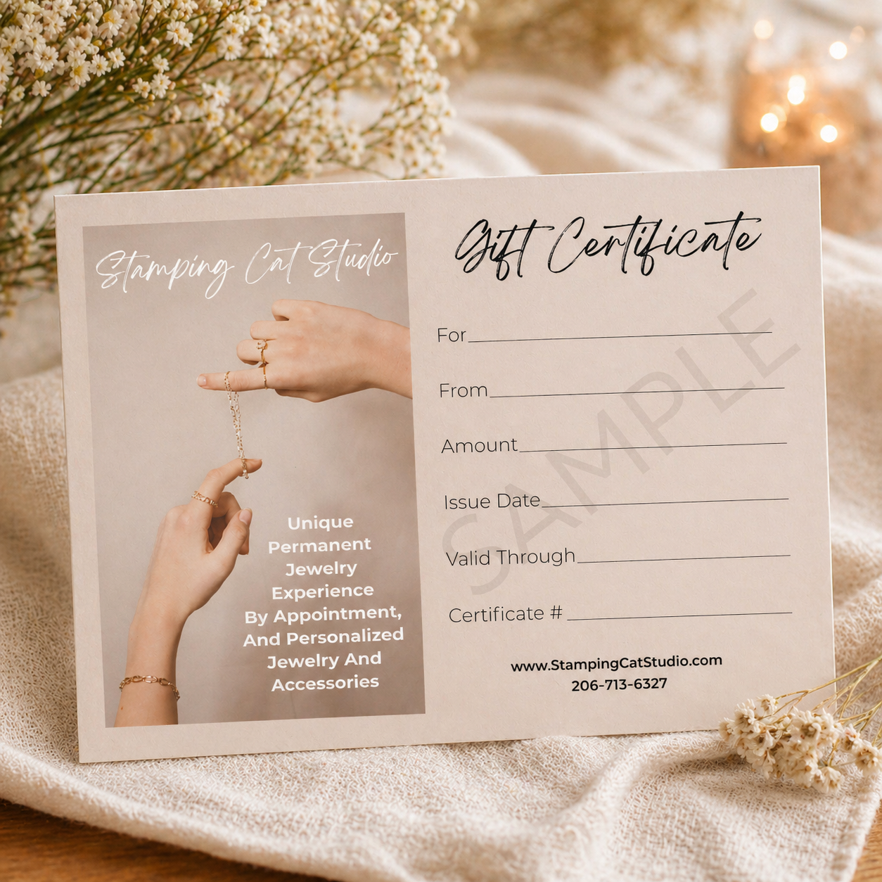 The May 8 gift cert from Stamping Cat Studio rests on beige fabric with white flowers. It features elegant fonts, jewelry art, fields for gift details, and includes contact info plus the website at the bottom. Read more at Stamping Cat Studio (stampingcatstudio.com).