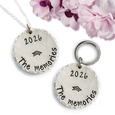 The Pers Graduation neck or key main features two round silver charms—one necklace, one key ring—engraved with "2026 The memories" and a graduation cap. Pink and purple faux flowers add a festive accent to this memorable graduation gift. Read more at Stamping Cat Studio (stampingcatstudio.com).